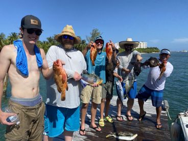 Group of anglers proudly displaying their catch, including colorful Snapper and Grouper, on a sunny day at the dock.
