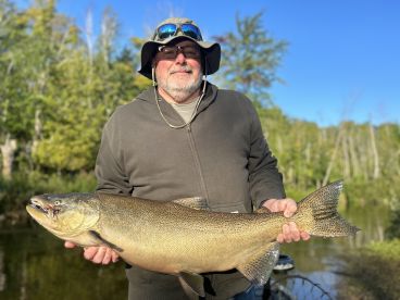 An angler proudly displaying a large Salmon caught during a serene fishing trip in a lush, green environment.