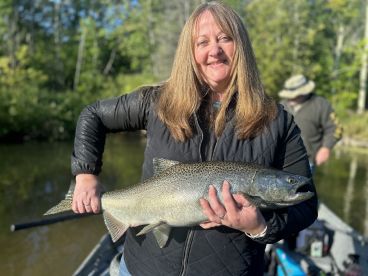An angler proudly displaying a large Salmon while fishing in a serene river setting.