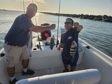 Two anglers proudly displaying their catch of striped bass while fishing from a boat in calm waters during sunset.