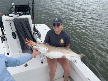 An angler proudly displaying a large Redfish while fishing on a boat, showcasing a successful catch in a coastal environment.