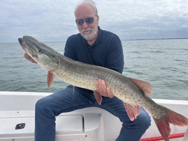 An angler proudly displays a large Northern Pike while seated on a boat, showcasing a successful fishing trip.