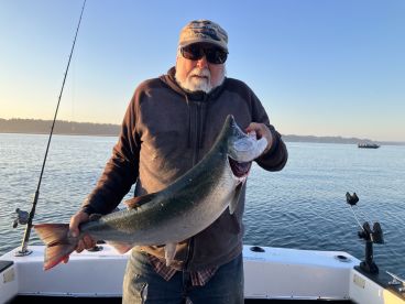 An angler proudly displaying a large Salmon while fishing on a boat in calm waters, showcasing a successful catch during a morning outing.