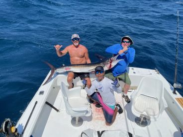 Three anglers proudly displaying a large Swordfish on a sport fishing boat, showcasing a successful deep-sea fishing trip.