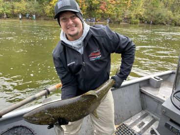 Angler proudly displaying a large Salmon while fishing from a boat in a scenic river setting.