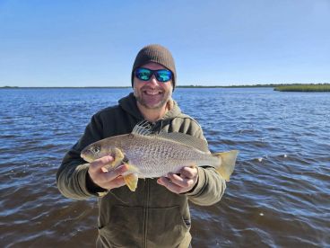 Angler proudly displaying a large Redfish while fishing in a scenic waterway.