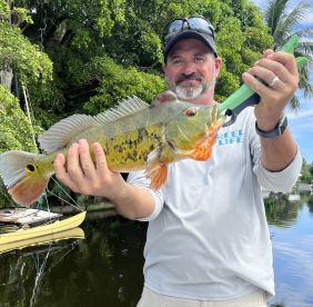 Angler proudly displaying a vibrant Peacock Bass caught in a scenic freshwater environment.