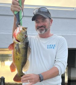 An angler proudly displaying a large Largemouth Bass caught during a fishing trip, showcasing the serene waters in the background.