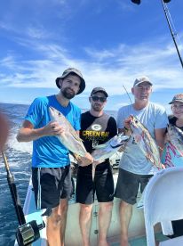 Group of anglers proudly displaying their catch of Yellowfin Tuna aboard a fishing charter in clear blue waters.