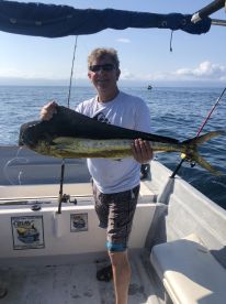 An angler proudly displaying a large Mahi-Mahi aboard a fishing boat in open waters.