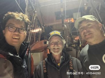 Three individuals posing for a selfie on a fishing boat at night, with fishing gear visible in the background.