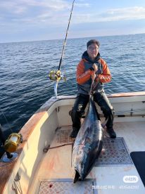 An angler proudly displaying a large Bluefin Tuna aboard a fishing boat, showcasing a successful deep-sea fishing trip.