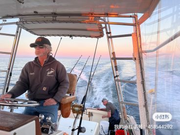 Two crew members aboard a charter boat navigating the calm waters during sunset, showcasing the helm and fishing rods in the background.
