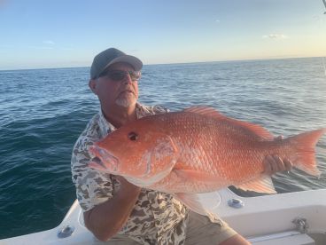 An angler proudly displaying a large Red Snapper while fishing offshore, showcasing a successful day on the water.