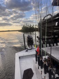 A view of the boat's interior showcasing fishing rods and a console as it navigates through a scenic waterway at sunset.