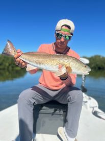 A young angler proudly displaying a Redfish while fishing in calm waters, showcasing a beautiful day on the water.