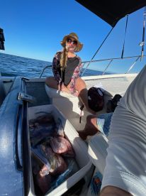 A woman sitting on a boat next to a cooler filled with neatly packed fish, enjoying a sunny day on the water.