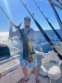 Angler proudly displaying a vibrant Mahi Mahi aboard a fishing boat in clear blue waters.