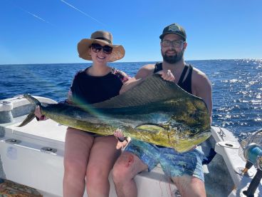 Two anglers proudly displaying a large Mahi-Mahi while fishing on a sunny day in open waters.