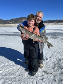 A young boy and his grandfather proudly display a Northern Pike while ice fishing in a snowy landscape.