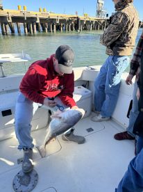 An angler on a boat is preparing to measure a large Redfish while others observe, showcasing the excitement of a fishing trip.