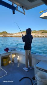 A young angler is actively reeling in a fish from a boat, surrounded by a scenic coastal backdrop.