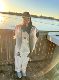 Angler proudly displaying two large striped bass at sunset, showcasing a successful fishing trip.