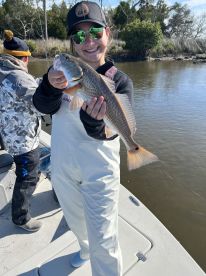 A young angler proudly displaying a Redfish while fishing from a boat in a scenic coastal environment.