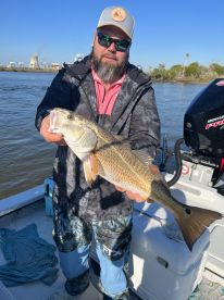 Angler proudly displaying a large Redfish while fishing from a boat in a scenic waterway.