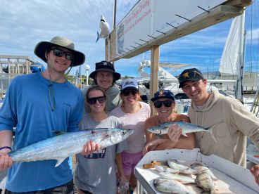 A group of anglers proudly displaying their catch, including a large King Mackerel and other fish, at the marina after a successful fishing trip.