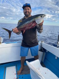 An angler proudly displaying a large Yellowfin Tuna aboard a fishing boat in open waters.