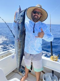 Angler proudly displaying a large Wahoo while fishing offshore, showcasing a sunny day on the water.