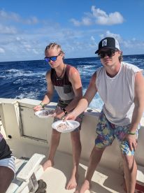 Two young anglers on a boat holding plates of fish, likely preparing for a meal after a fishing trip.