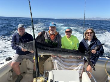 A group of four anglers proudly displaying a large Marlin aboard their boat during a deep-sea fishing trip.
