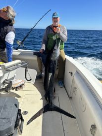 An excited angler proudly displaying a large Swordfish aboard a fishing boat in open waters.
