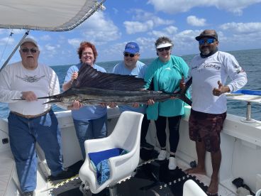A group of anglers proudly displaying a large Sailfish aboard a charter boat, enjoying a successful day of fishing in open waters.