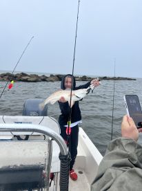 A young angler proudly displaying a large Redfish while fishing from a boat, with rocky formations in the background.