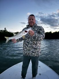 Angler holding a large Snook while standing on the bow of a boat during a sunset fishing trip.
