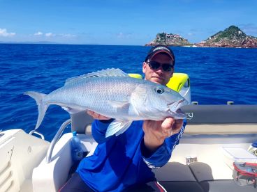 Angler displaying a large Snapper while fishing near scenic islands in clear blue waters.