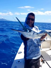 Angler proudly displaying a large Sailfish while fishing offshore, showcasing a beautiful blue ocean backdrop.