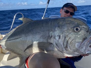 Angler proudly displaying a large Giant Trevally while fishing offshore, showcasing the thrill of deep-sea fishing.