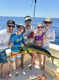 A family group proudly displaying a large Mahi-Mahi while fishing in open waters, showcasing a fun day on the boat.