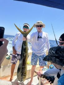 Two anglers proudly displaying a large Mahi Mahi aboard a fishing boat, enjoying a successful day on the water.
