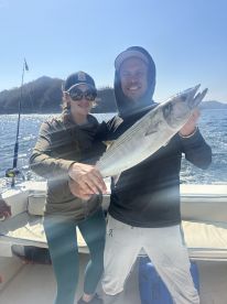 Two anglers proudly displaying a large fish while enjoying a sunny day on the water.
