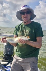 An angler proudly displaying a Speckled Trout while fishing on a boat in coastal waters.