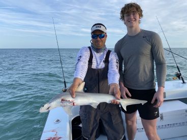 Two anglers proudly displaying a caught shark while fishing on a boat in open waters.