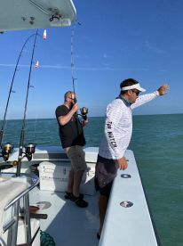 Two anglers actively fishing from a boat, with one casting while the other prepares to reel in. The scene captures the excitement of a fishing trip in open waters.