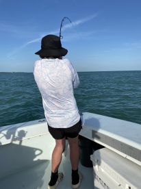 A young angler is actively reeling in a fish while fishing on a boat in open waters, showcasing the excitement of the catch.
