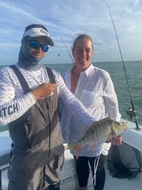Two anglers proudly displaying a colorful Snapper while fishing on a boat in clear waters.