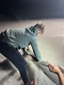 A young angler assisting in the catch of a large fish on the beach during a nighttime fishing adventure.
